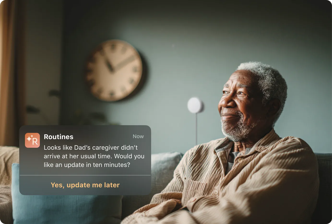 An elderly man sits calmly on a couch with a white sensor and clock on the wall behind him, while a notification from the Routines app alerts that his caregiver hasn't arrived at the usual time, offering a follow-up update.